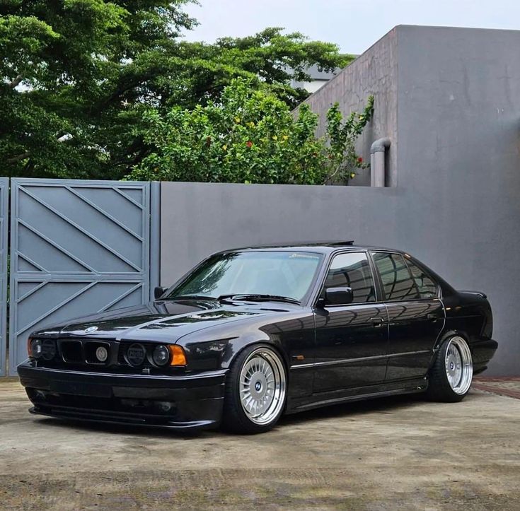 a black car parked in front of a gray wall with trees and bushes behind it