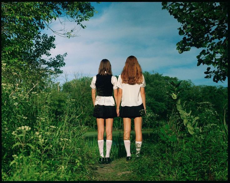 two young women walking down a path in the woods with their backs to each other