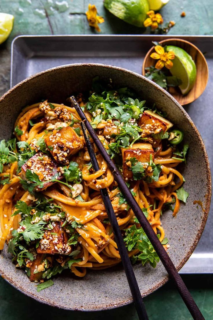 a bowl filled with noodles and vegetables next to chopsticks on a tray,