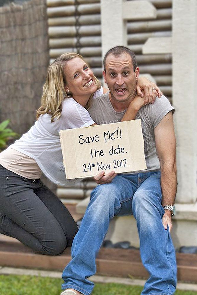 a man and woman holding a sign that says save me the date