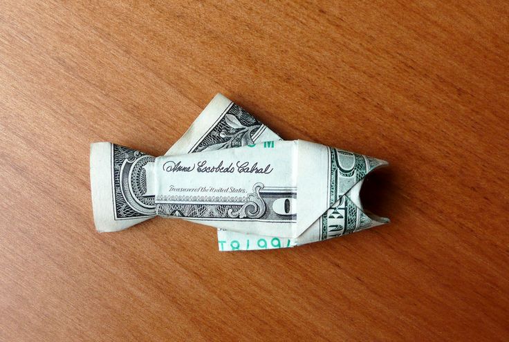 an origami dollar bill folded into a paper boat on top of a wooden table