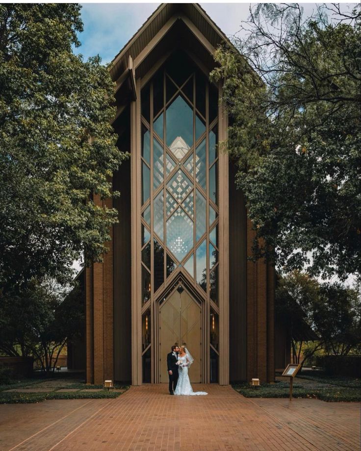 a bride and groom standing in front of a tall building with large windows on each side