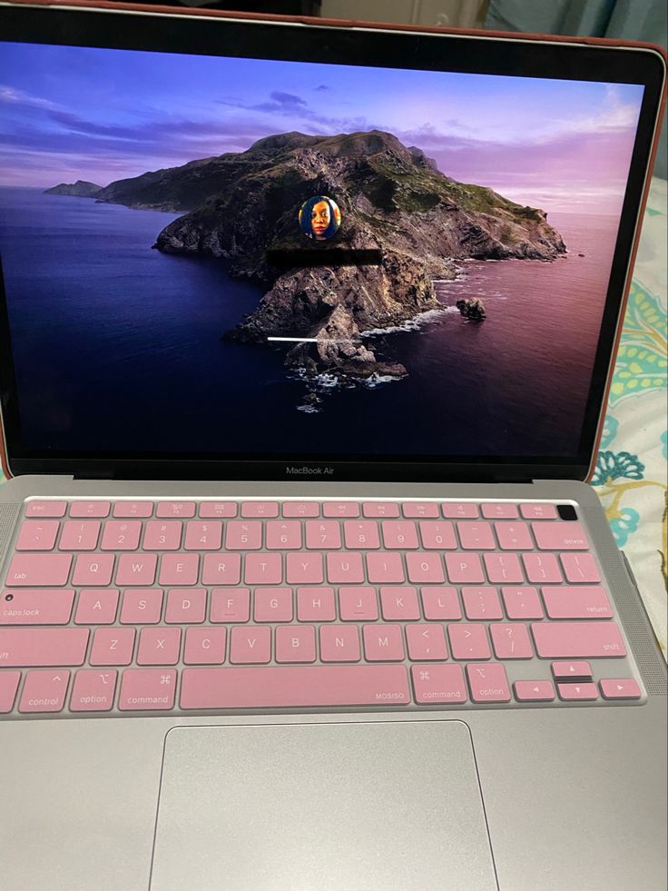 an open laptop computer sitting on top of a bed next to a pink mouse and keyboard