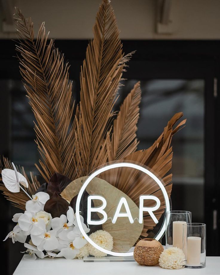 a bar sign sitting on top of a white table next to flowers and candle holders