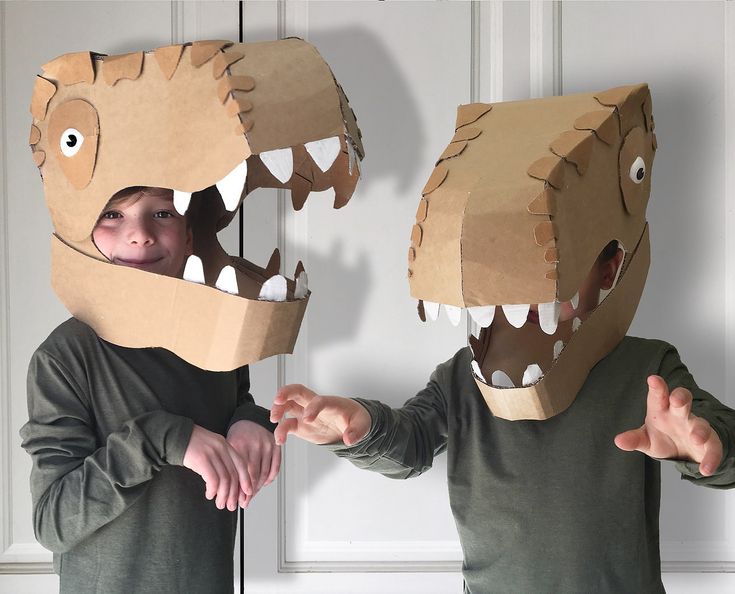 two children wearing cardboard dinosaurs masks with their mouths open and hands out to each other