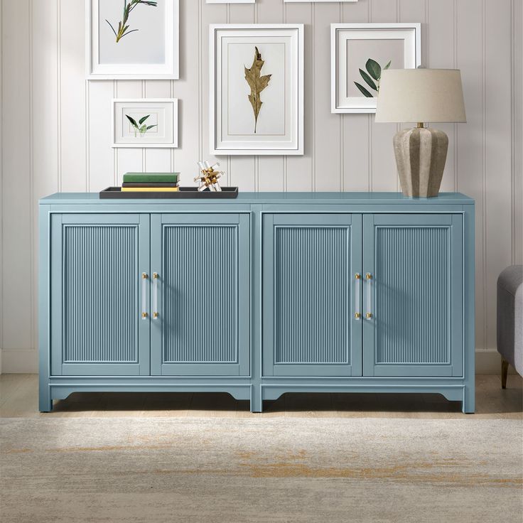 a blue sideboard in a living room with framed pictures on the wall and a lamp