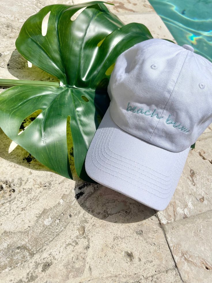 Beach bum dad hat. White dad hat, unstructured. 100% cotton, adjustable closure. One size fits most. Embroidered words in light blue. Trendy Cotton Baseball Cap For Vacation, Gray Baseball Cap For Summer Beach, Cotton Trucker Hat For The Beach, Gray Curved Brim Baseball Cap For Summer, Beach Letter Print Cotton Baseball Cap, Trendy Cotton Hat For Vacation, Trendy Dad Hat Baseball Cap For Vacation, Trendy Cotton Dad Hat For Vacation, Light Blue Cotton Hat With Curved Brim