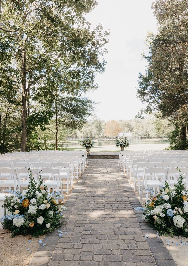 an outdoor ceremony set up with white chairs and flowers