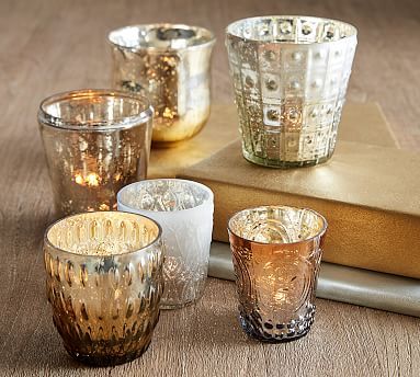 five different colored glass cups sitting on top of a table next to a book and candle holder