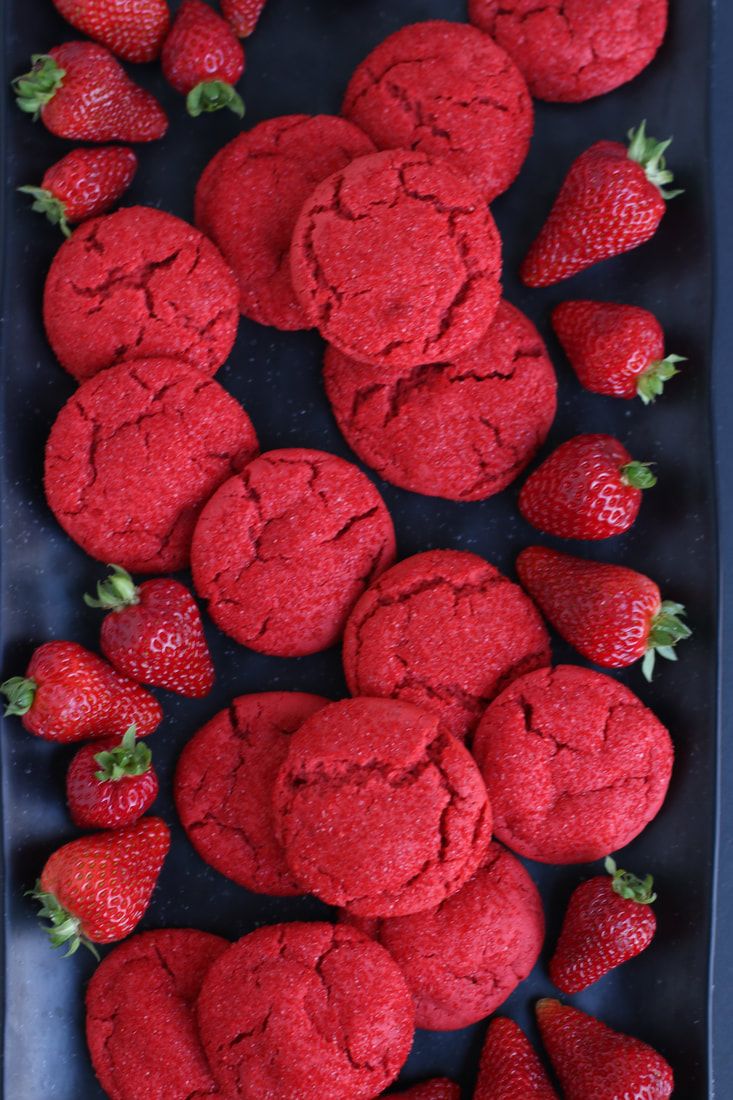 red cookies and strawberries are arranged on a black tray, ready to be eaten