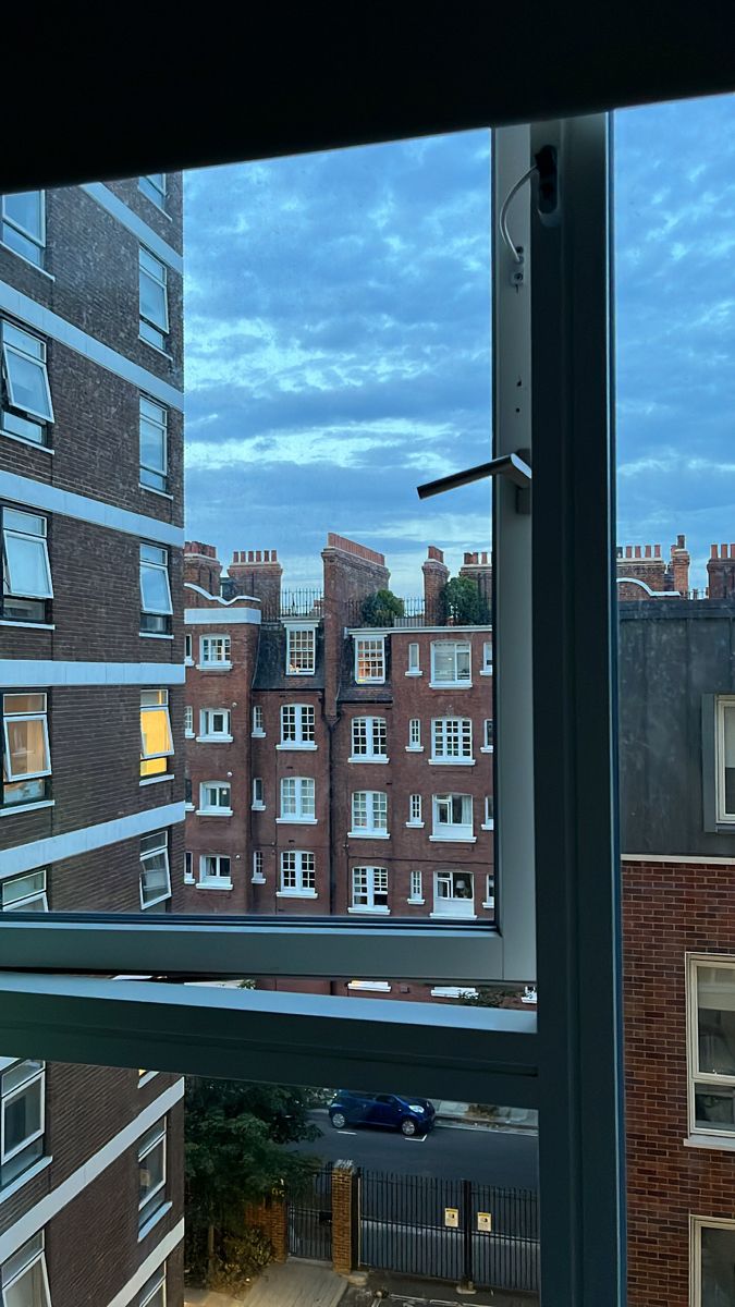 an open window looking out onto a city at night with buildings in the distance and blue sky