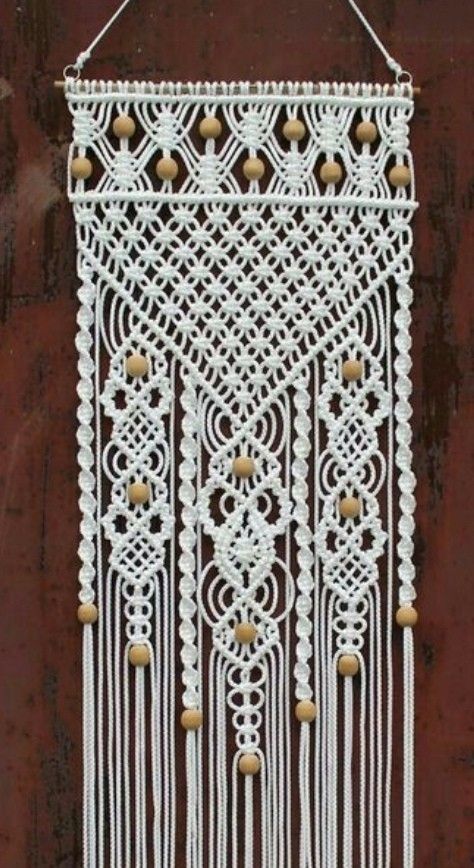 a white macrame hanging on the side of a building with bells and beads