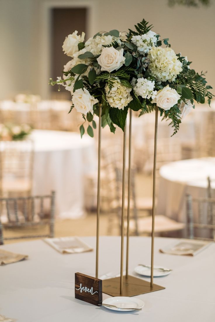 there are two tall vases with white flowers on the table at this wedding reception