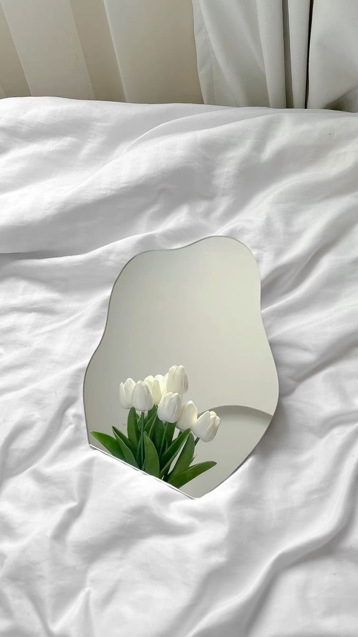 there is a mirror on the bed with white flowers in front of it and an image of tulips