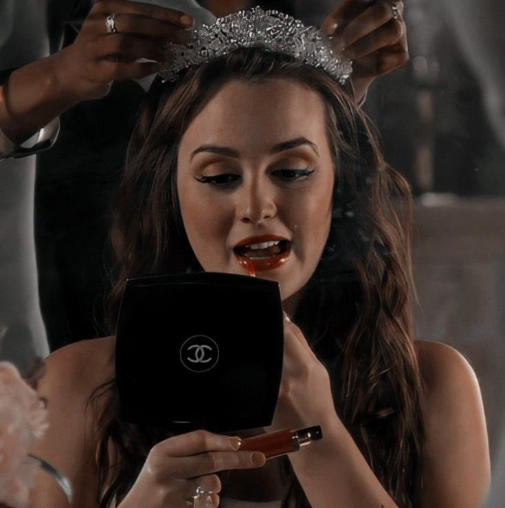 a woman in a tiara looking at her cell phone while she is getting ready to brush her hair