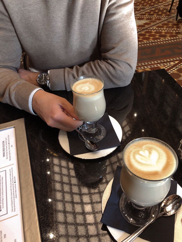 two cups of coffee sitting on top of a table next to each other, one with a latte in it