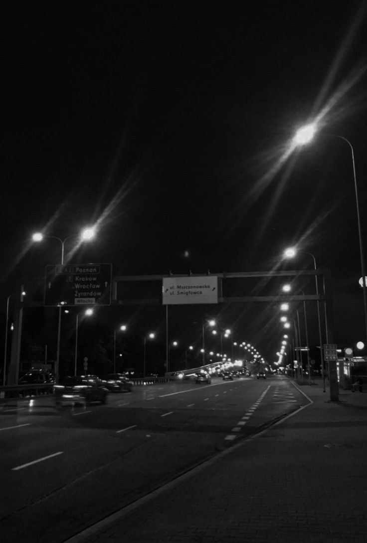 black and white photo of street lights at night with cars driving on the road below