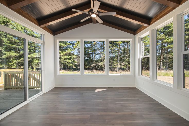 an empty room with large windows and wood flooring on the outside, looking out onto trees