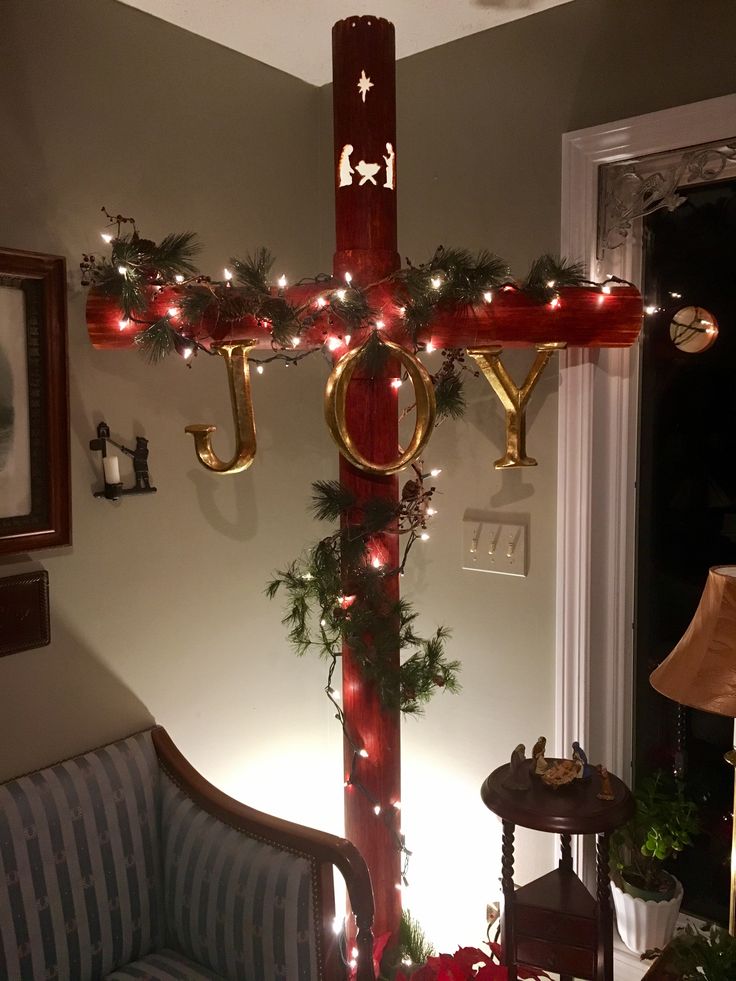 a cross decorated with christmas lights in the corner of a room next to a couch