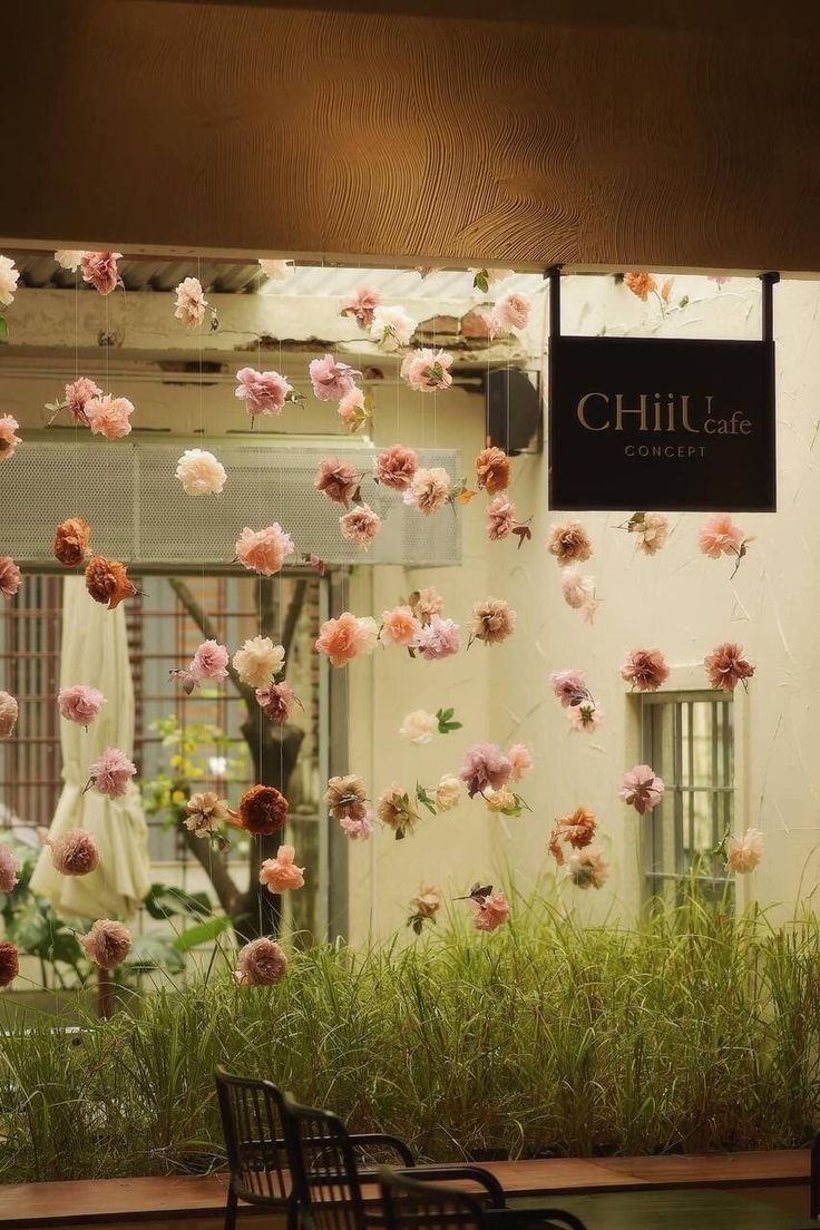 flowers are hanging from the ceiling in front of a building with chairs and tables outside