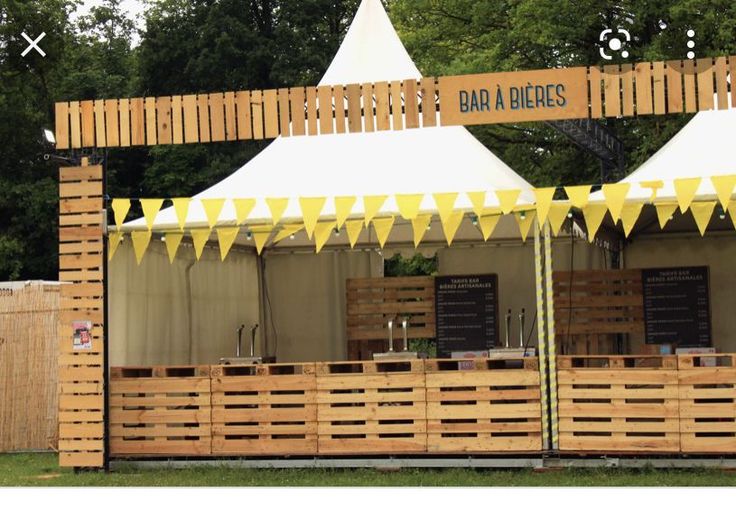 an outdoor food stand with yellow and white flags on the top, along with wooden pallets