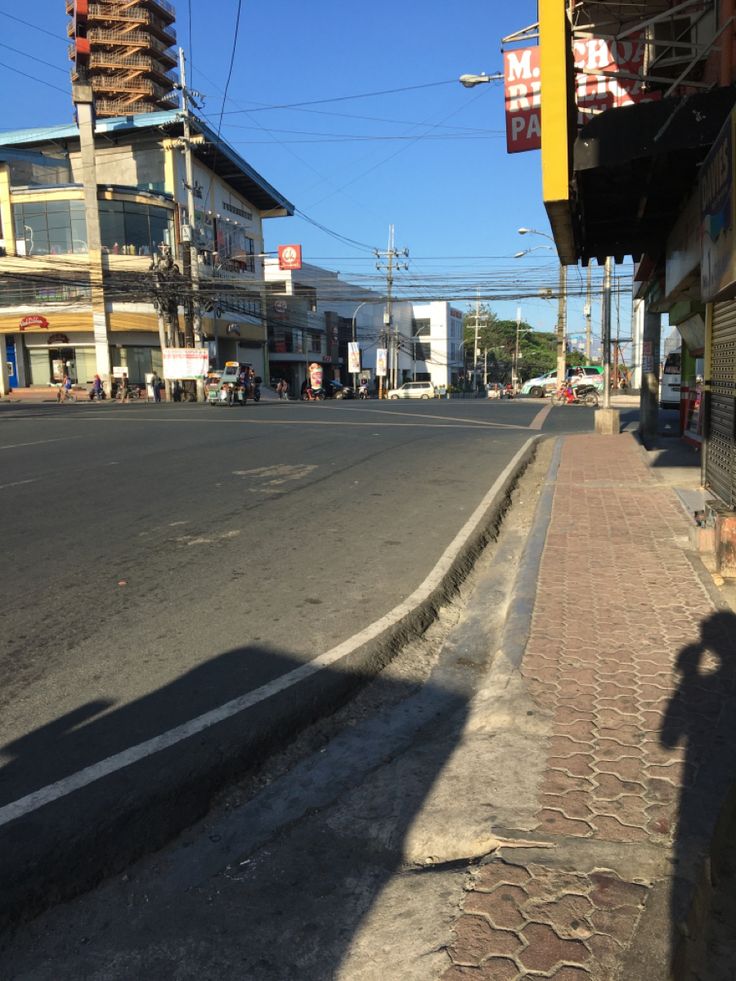 the shadow of a person walking down an empty street with buildings in the background on a sunny day