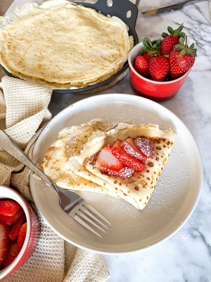 a plate with pancakes and strawberries on it next to a bowl of strawberries