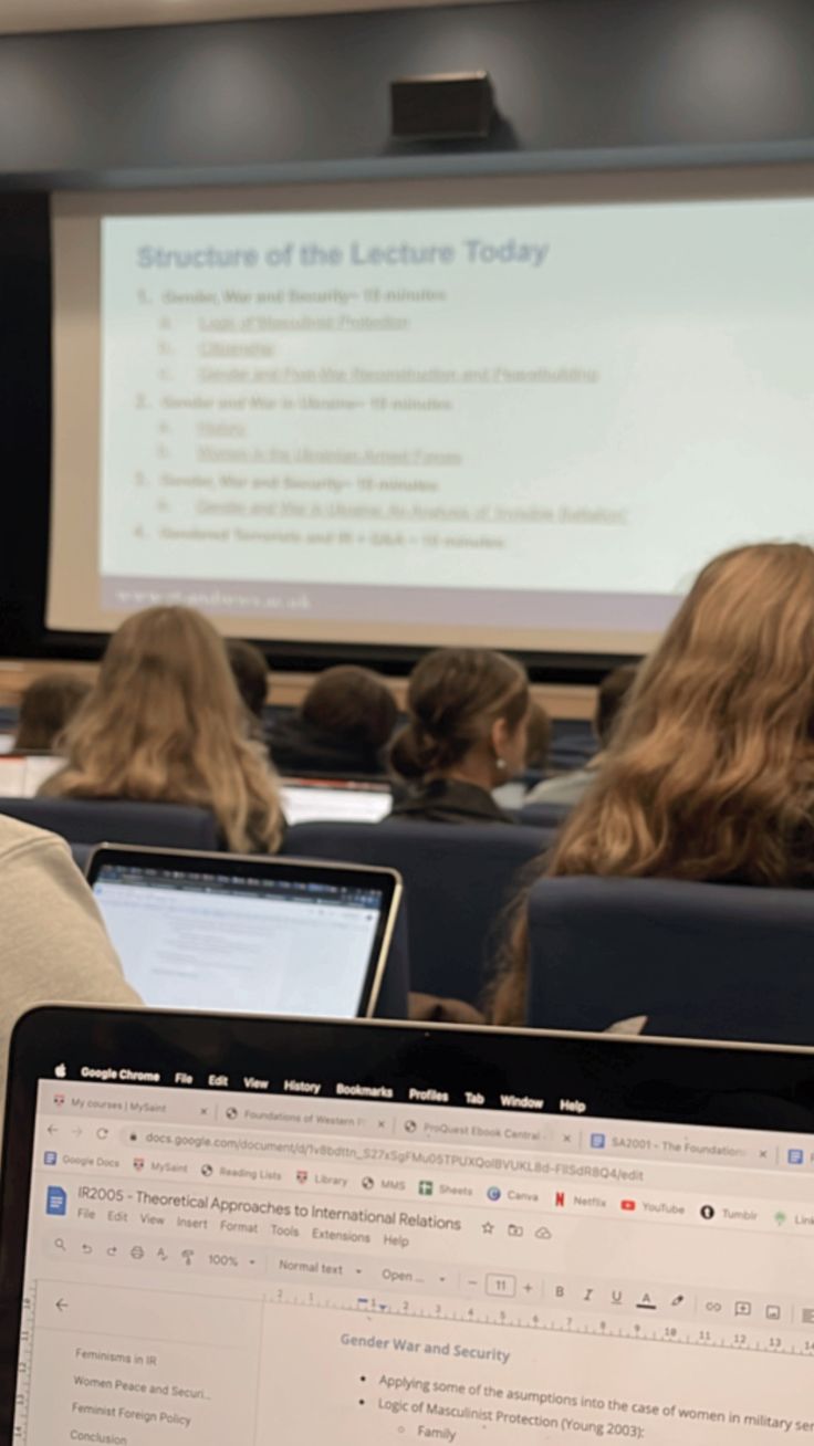 people sitting at desks in front of laptop computers with projector screen behind them