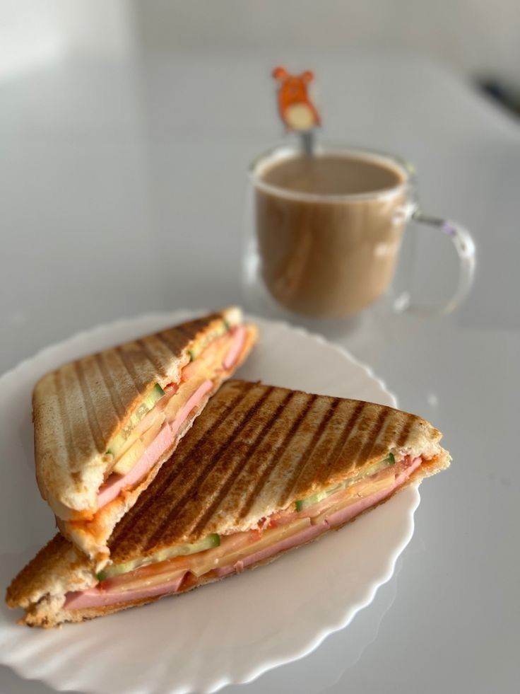 a sandwich cut in half sitting on top of a white plate next to a cup of coffee