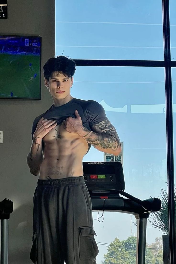 a shirtless man standing in front of a treadmill and looking at the camera