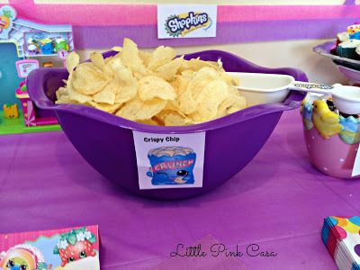 a purple bowl filled with chips sitting on top of a table next to cupcakes