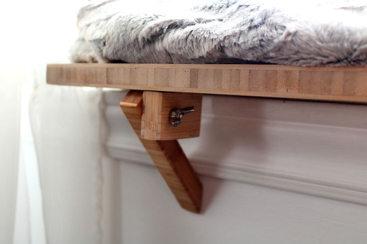 a wooden shelf with a fur covered pillow on it's top, and a white wall in the background