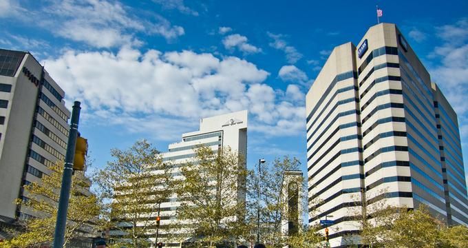 people are walking on the sidewalk in front of some tall buildings with trees and bushes