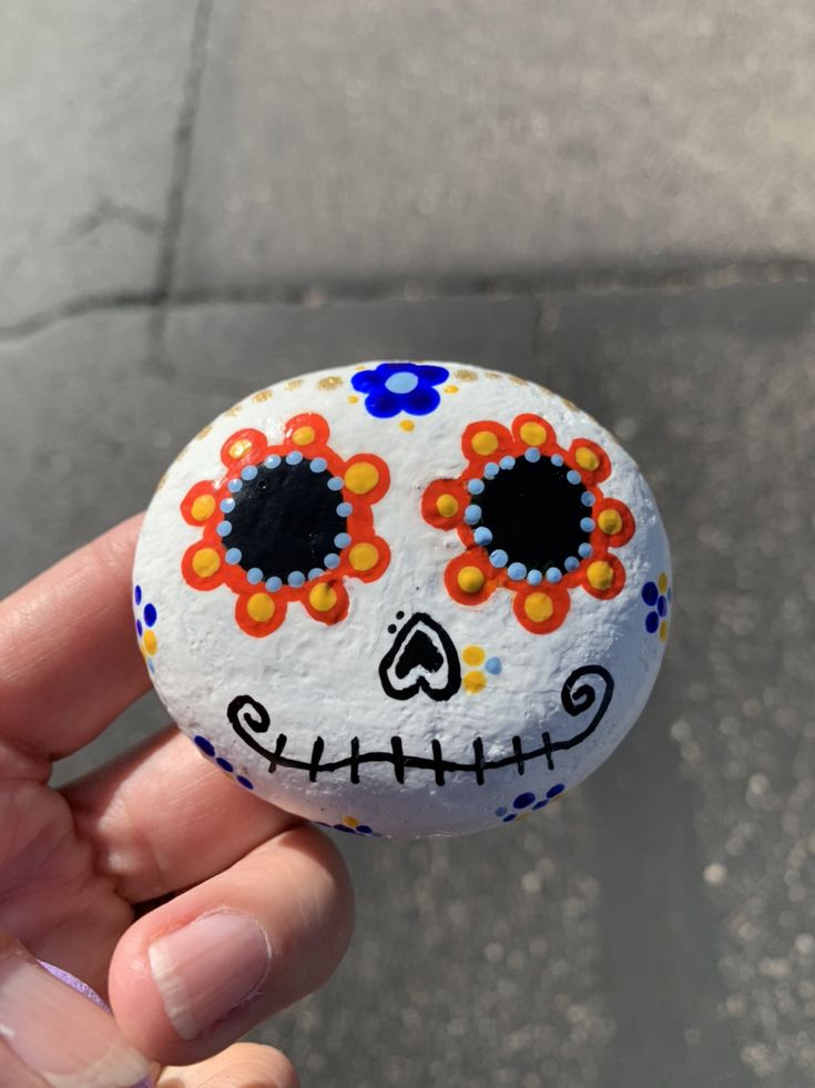 a hand holding a rock with a painted skull on it's face and eyes