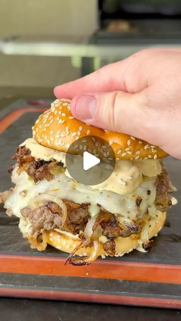 a hamburger with cheese and meat on it being held by someone's hand over an orange tray