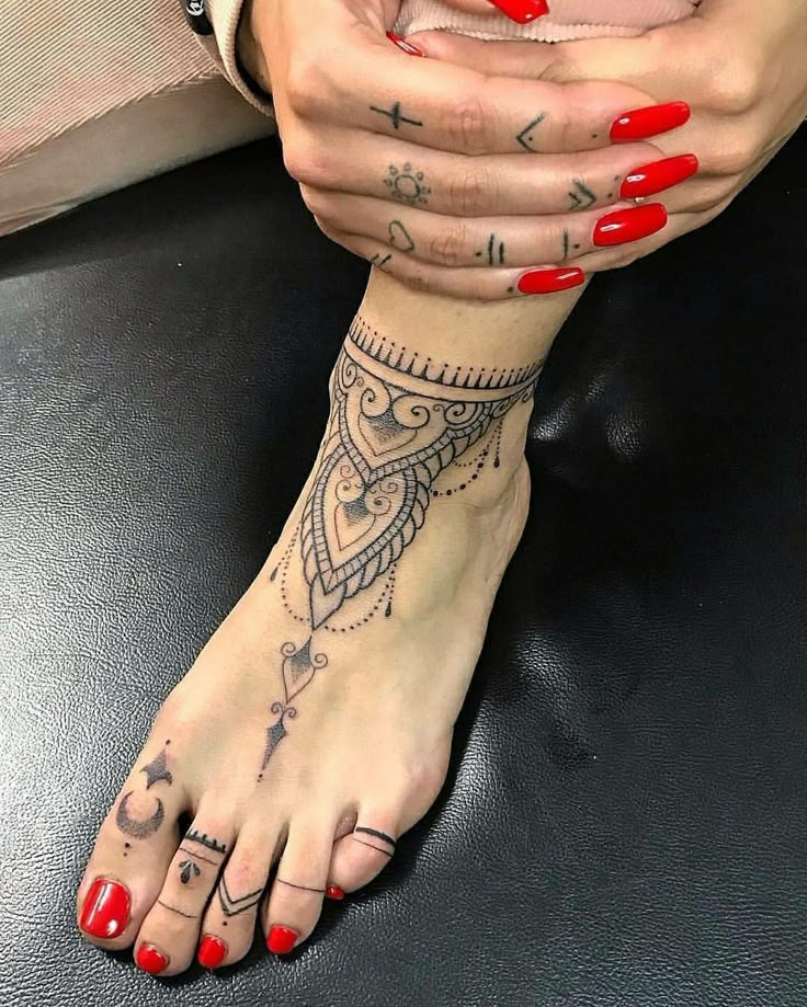 a woman's foot with tattoos and red nail polishes on her toes, sitting on a black leather surface