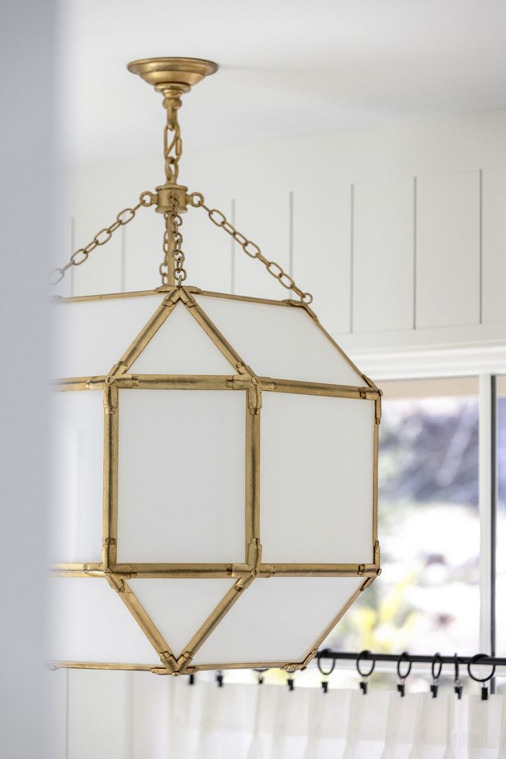 a white and gold chandelier hanging from the ceiling in a room with windows