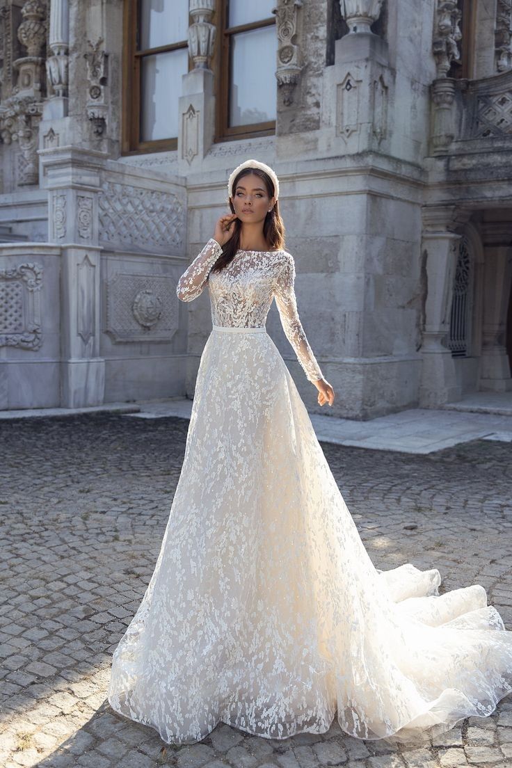 a woman in a white wedding dress standing on a cobblestone street with an old building in the background