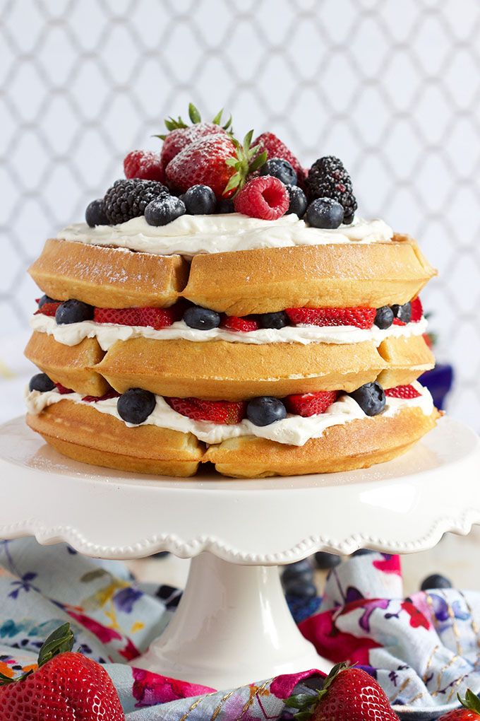 a stack of pancakes topped with berries and whipped cream on a white cake platter