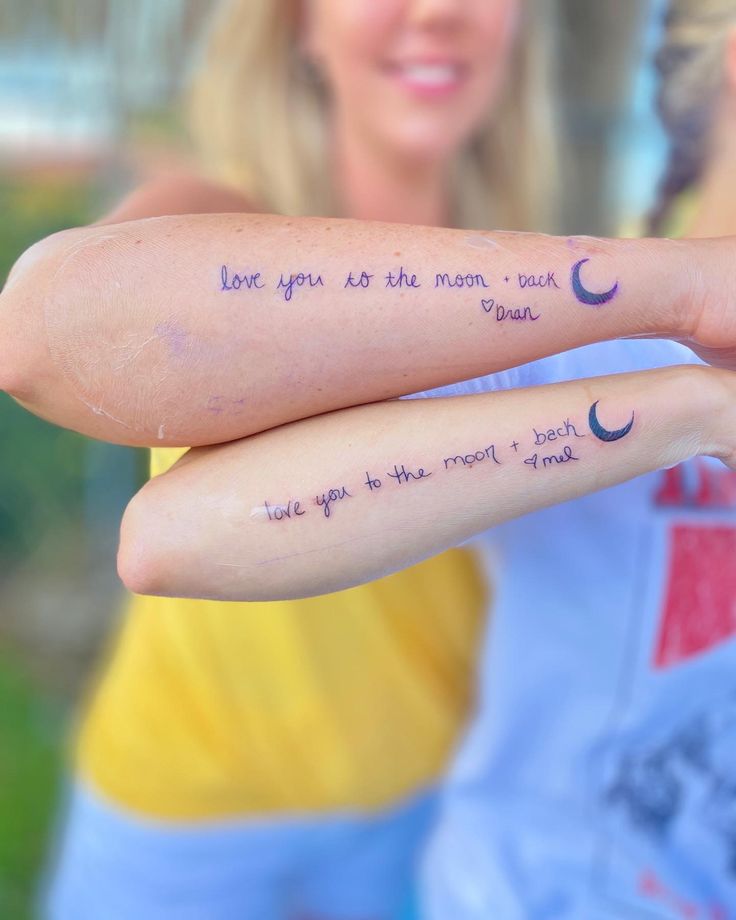 two women with tattoos on their arms holding each other's fingers and saying love you are the moon