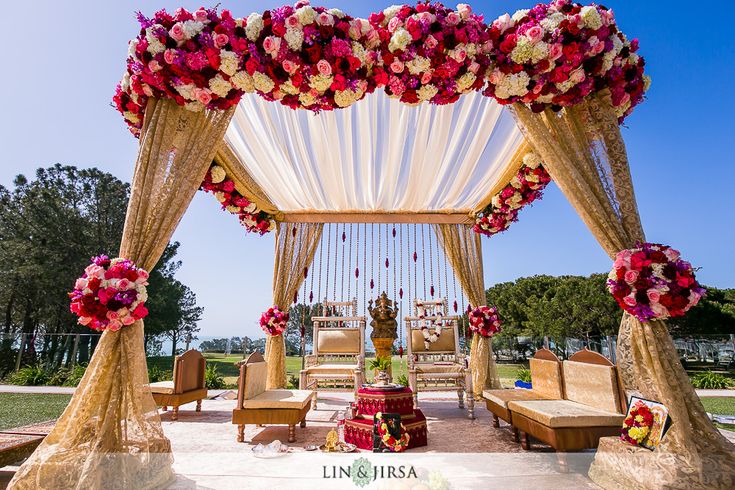 an outdoor wedding setup with red and white flowers on the canopy, couches and tables