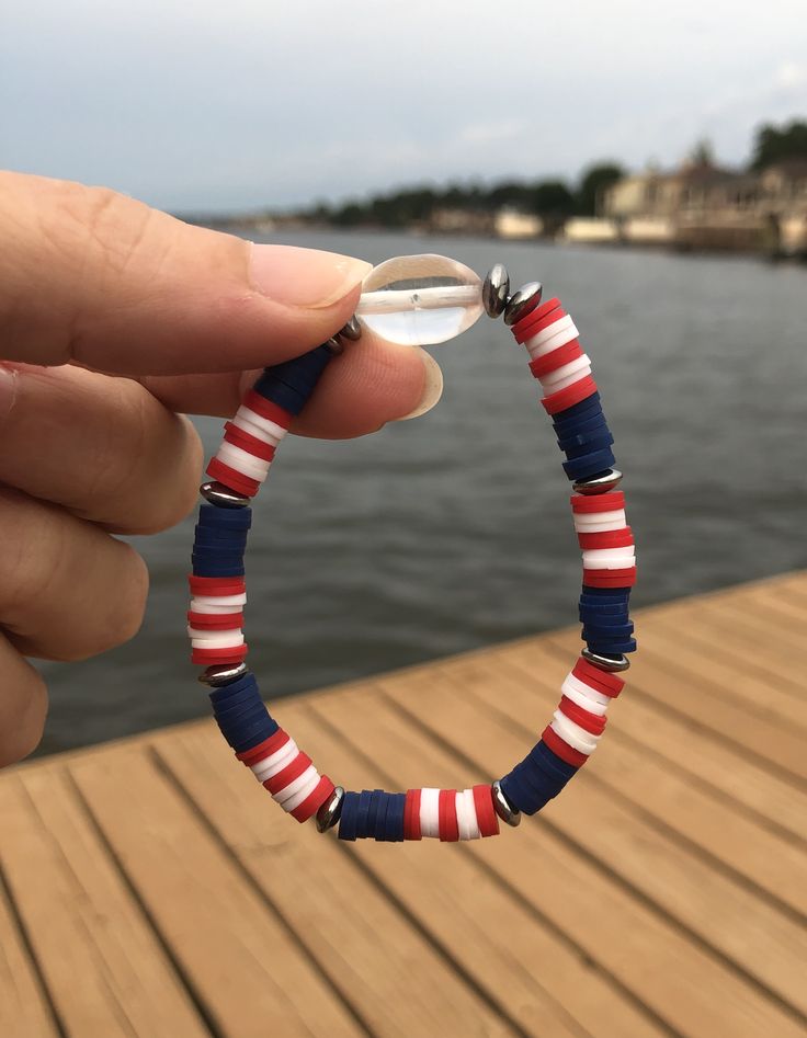 a hand holding a beaded bracelet on a wooden dock next to a body of water