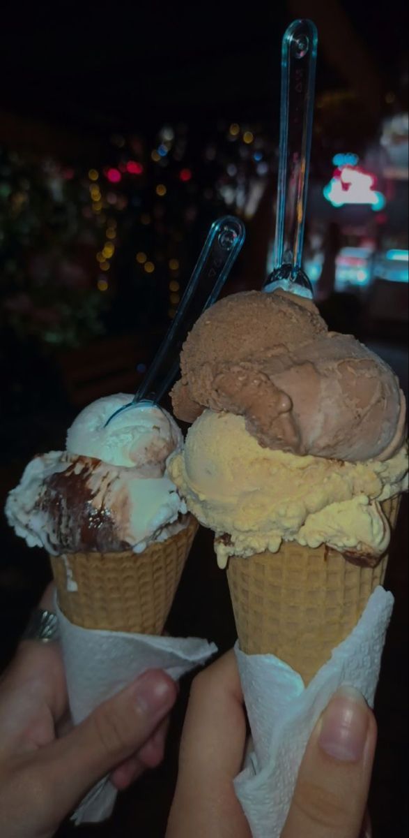 two ice cream cones with chocolate and vanilla on top are being held up by someone's hand