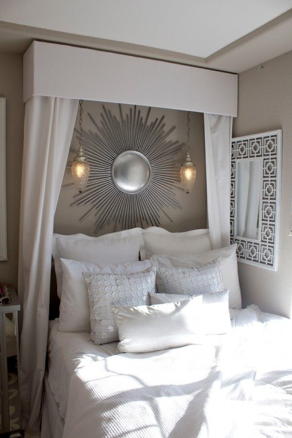 a bed with white sheets and pillows in a bedroom next to a mirror on the wall