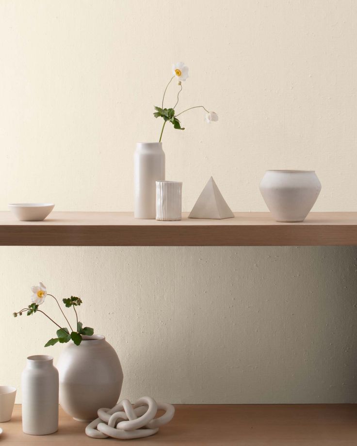 three white vases with flowers in them on a wooden shelf next to other items