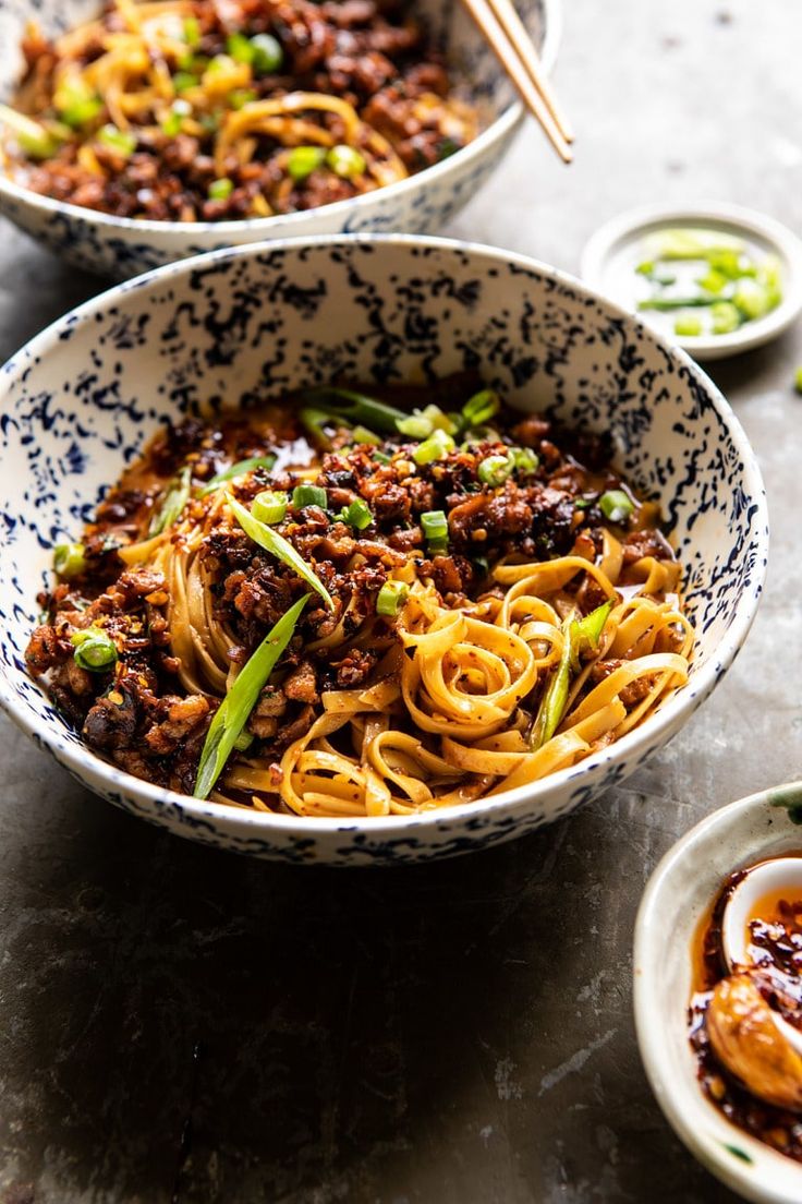 two bowls filled with noodles and meat on top of a table next to dipping sauces