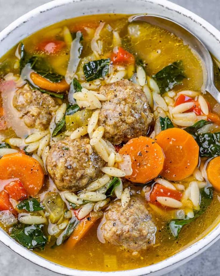 a white bowl filled with meatballs, pasta and veggie soup on top of a table