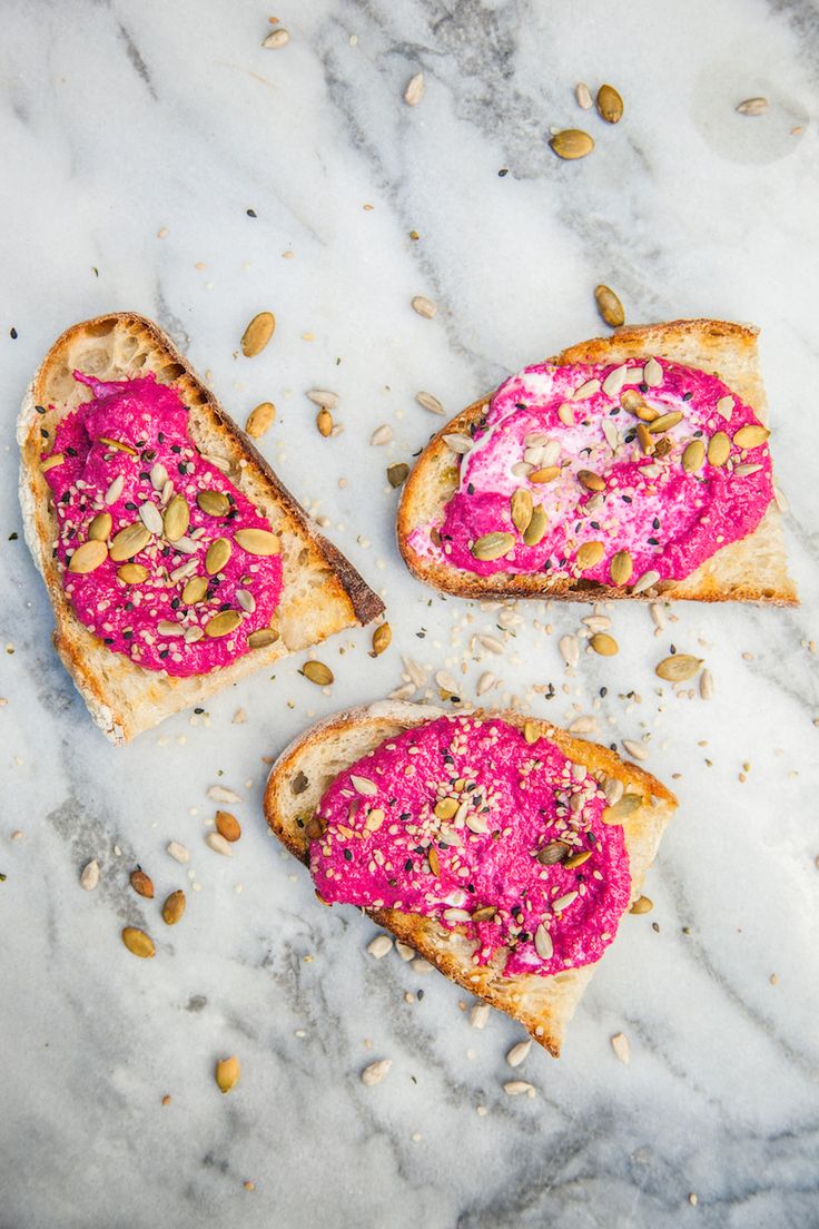 three pieces of bread with pink toppings and nuts on them sitting on a marble surface