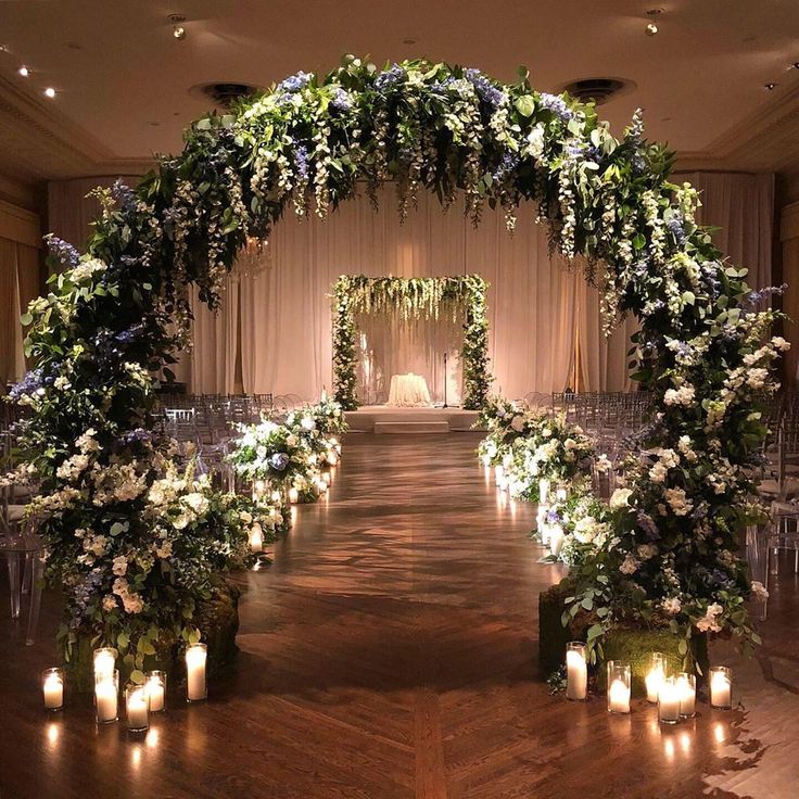 a wedding ceremony with candles and flowers on the aisle in front of an arch decorated with greenery