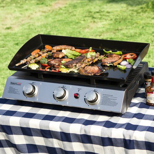 a bbq grill with food on it sitting in front of a picnic table covered in blue and white checkered cloth